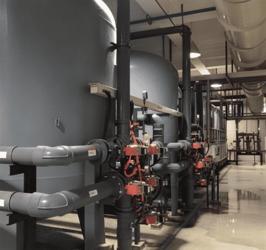 An industrial CPVC piping system installed in a water treatment plant, featuring automated pneumatic valves, grey CPVC pipes, and large filtration tanks